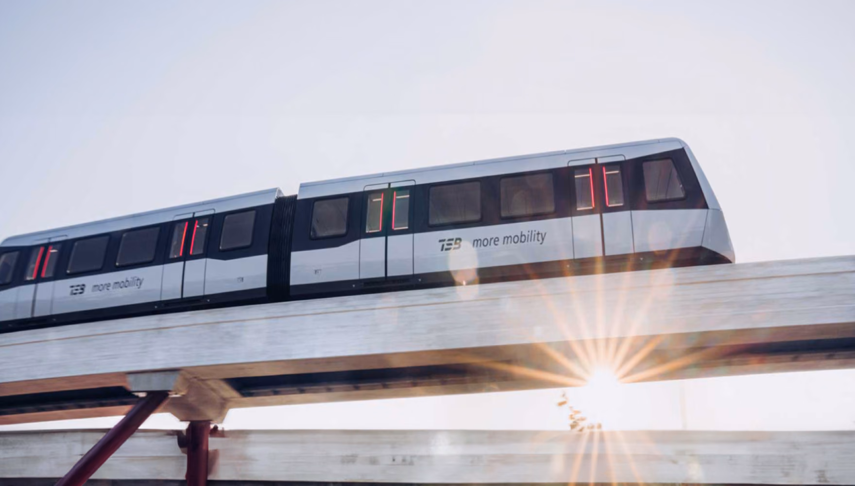 A white TSB maglev train stands on an elevated concrete guideway, the low sun flaring beneath the beam.