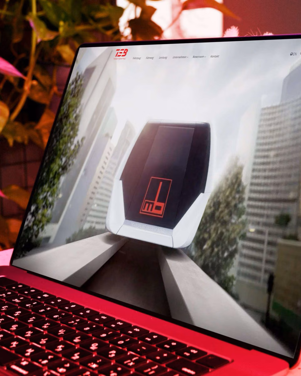 A laptop in red light shows the TSB site with a head-on render of the maglev vehicle between city towers.