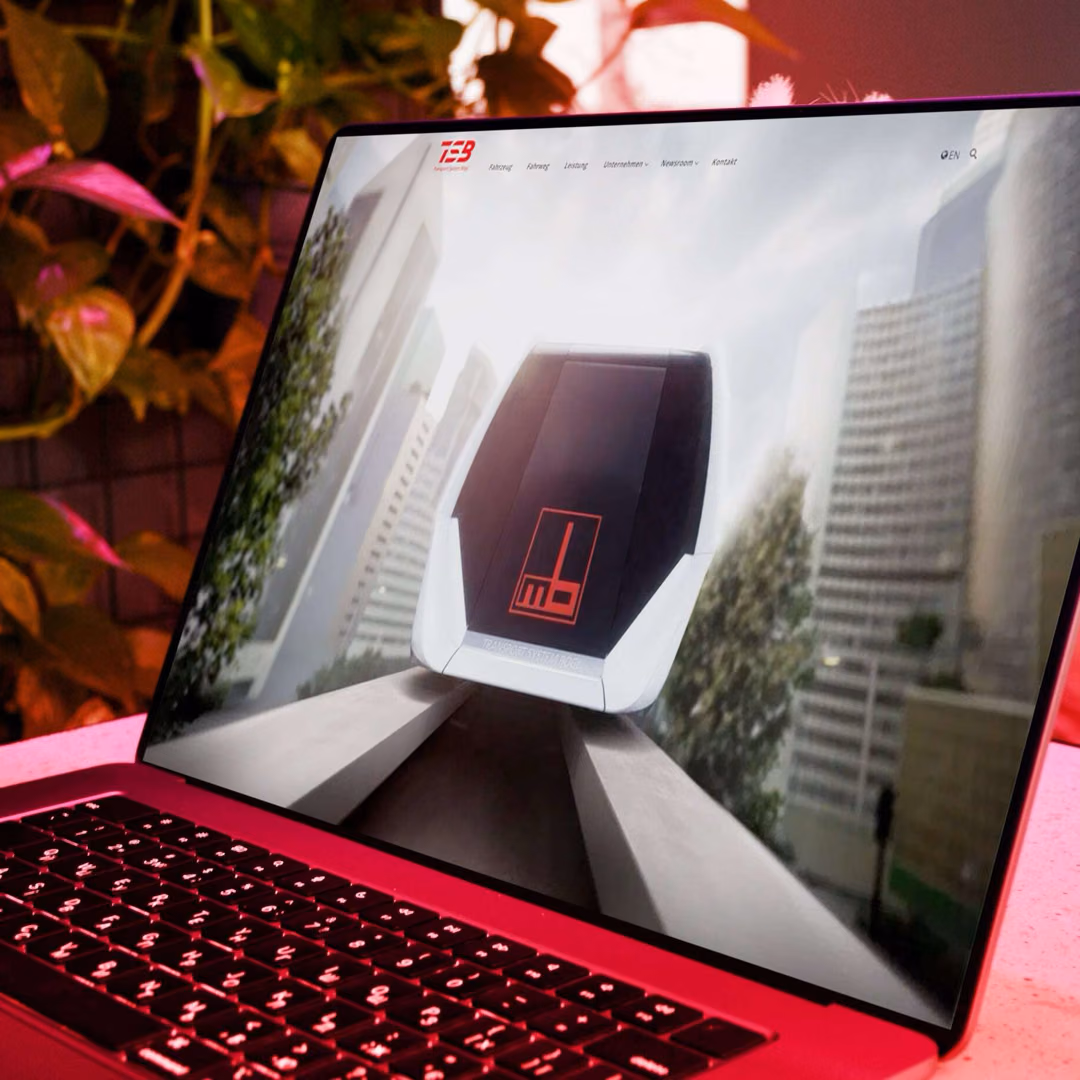 A laptop in red light shows the Transport System Boegl site with a head-on render of the maglev vehicle running between city towers.