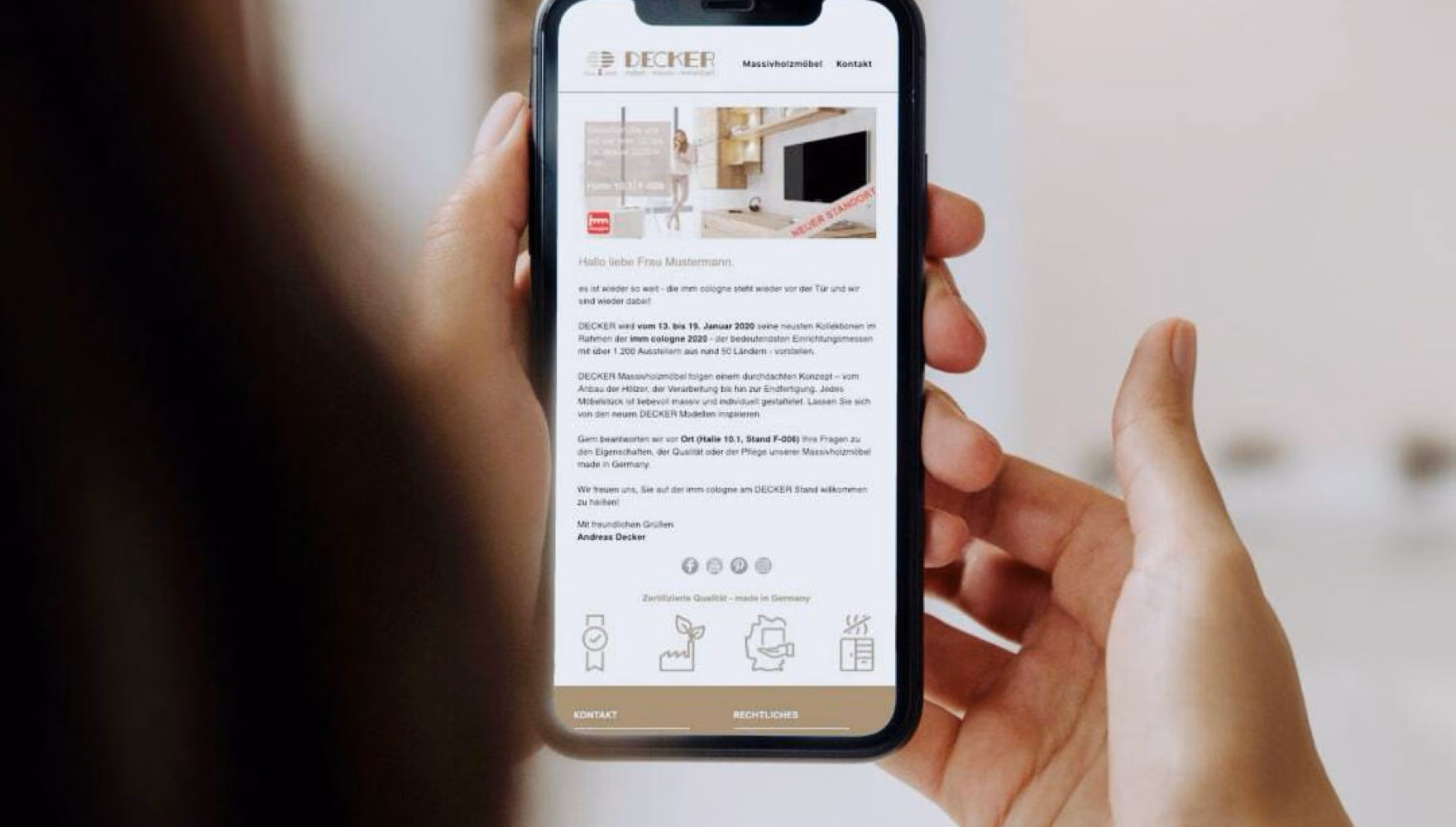 Hands hold a phone showing a Decker e-mail newsletter that greets a sample recipient by name and invites her to the company's trade fair stand.