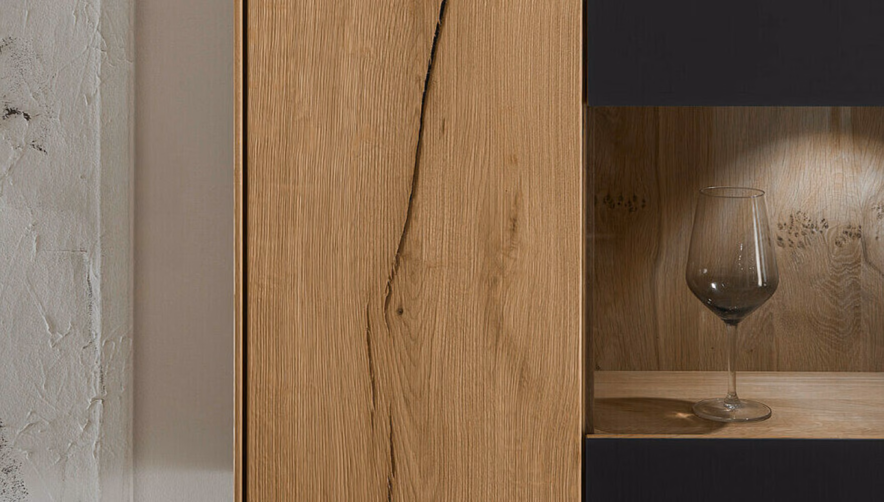 An oak cabinet front with a dark vertical joint running down the grain, next to a lit glass niche holding a wine glass.