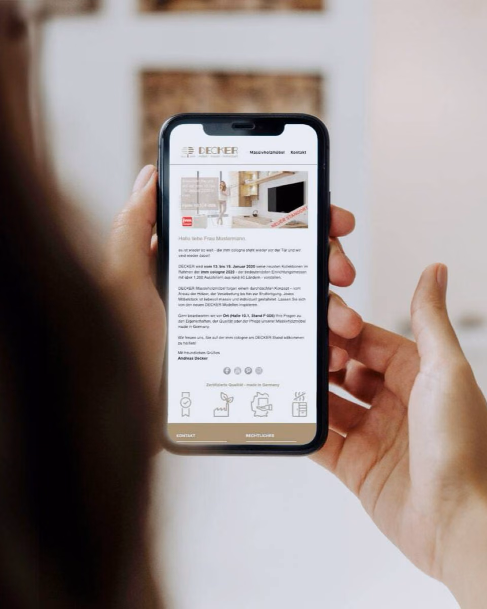 Hands hold a phone showing a Decker e-mail newsletter that greets a sample recipient by name and invites her to the company's trade fair stand.