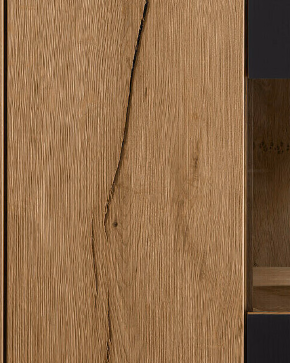 An oak cabinet front with a dark vertical joint running down the grain, next to a lit glass niche holding a wine glass.