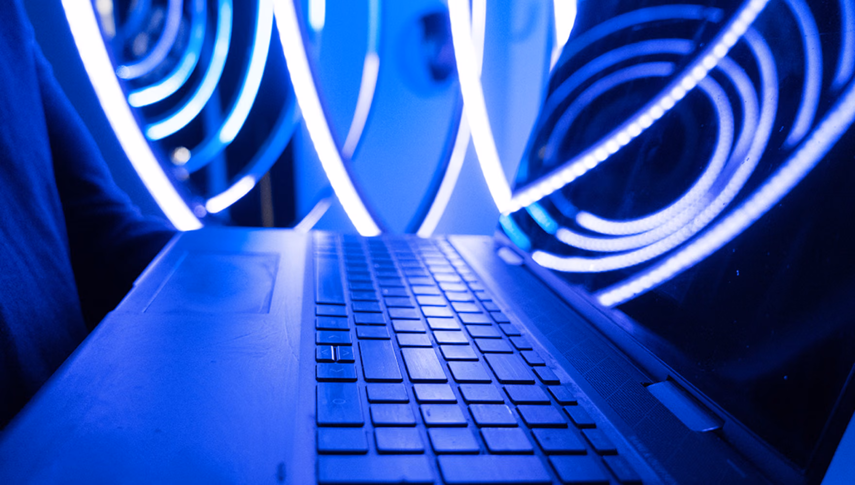An open laptop held in front of concentric spirals of blue neon light.
