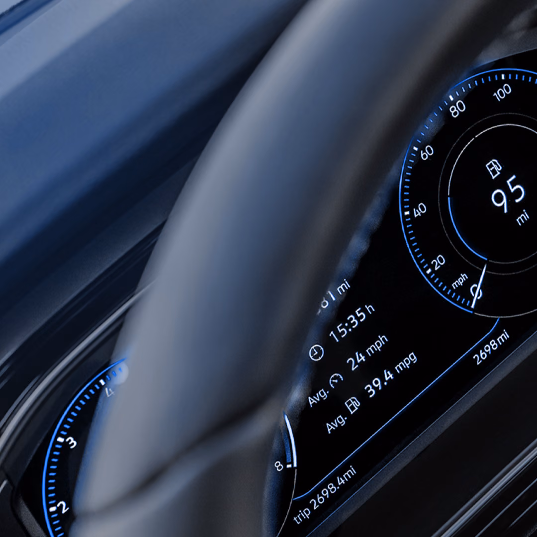 A car's digital instrument cluster glows blue behind the rim of the steering wheel, showing remaining range and trip figures.
