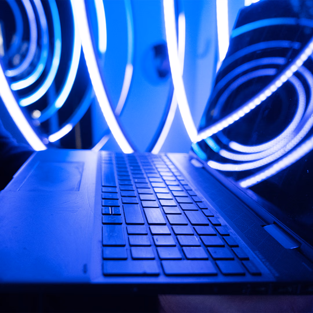 An open laptop held in front of concentric spirals of blue neon light.