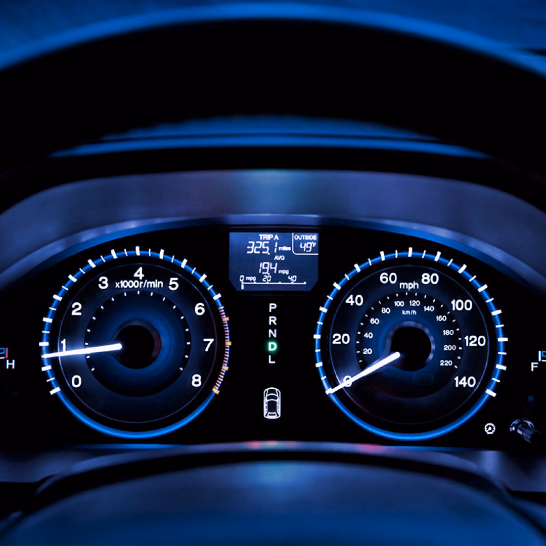 A car dashboard at night, tachometer and speedometer lit in blue either side of a small trip display.