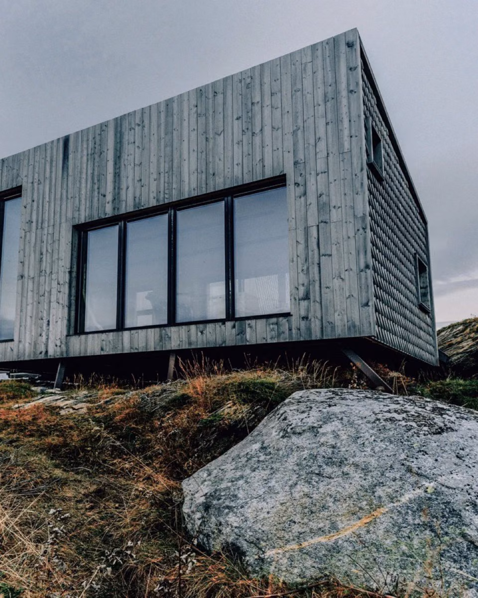 A timber-clad house with large windows on a hillside at dusk.