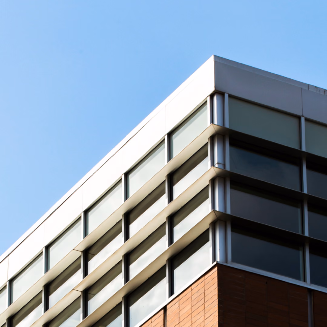 The top corner of an office building with banded glazing and brick cladding stands against a clear blue sky.