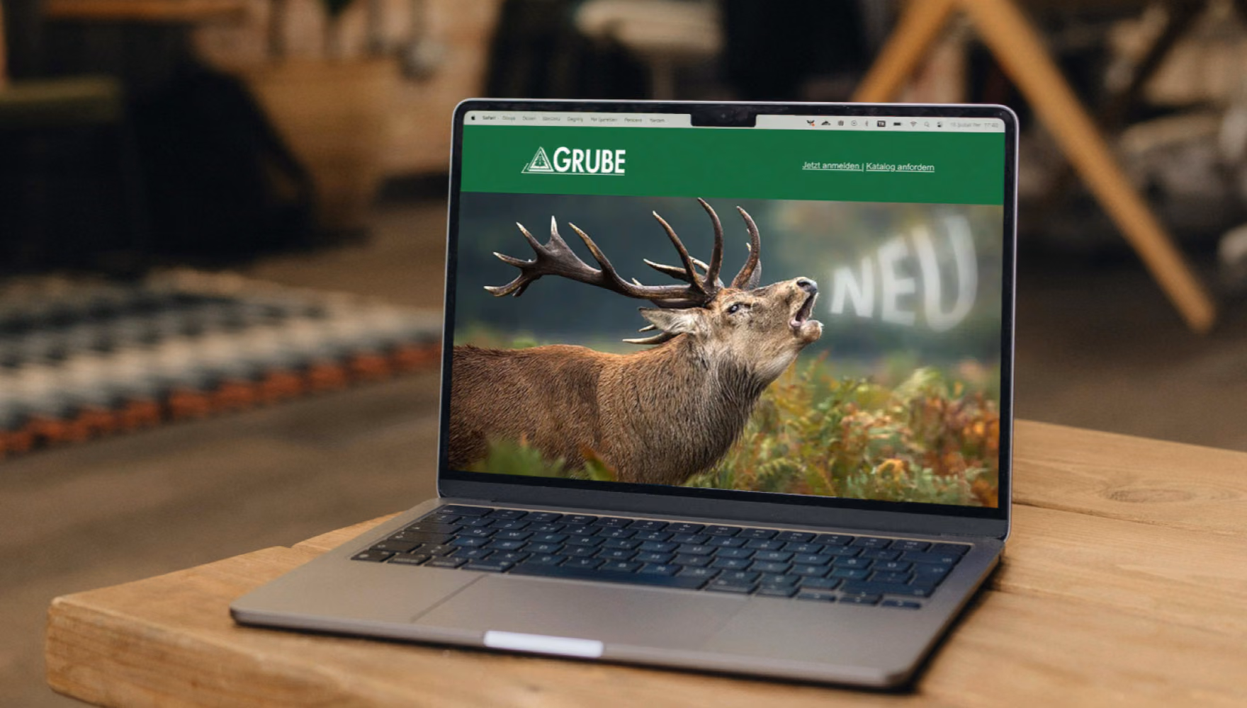 A laptop on a wooden table shows the Grube online shop, its homepage filled by a roaring red stag.