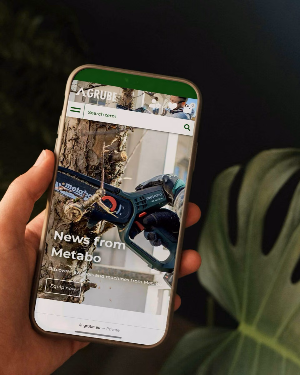 A hand holds a phone showing Grube's mobile shop, where a chainsaw cuts into a trunk under the headline News from Metabo.