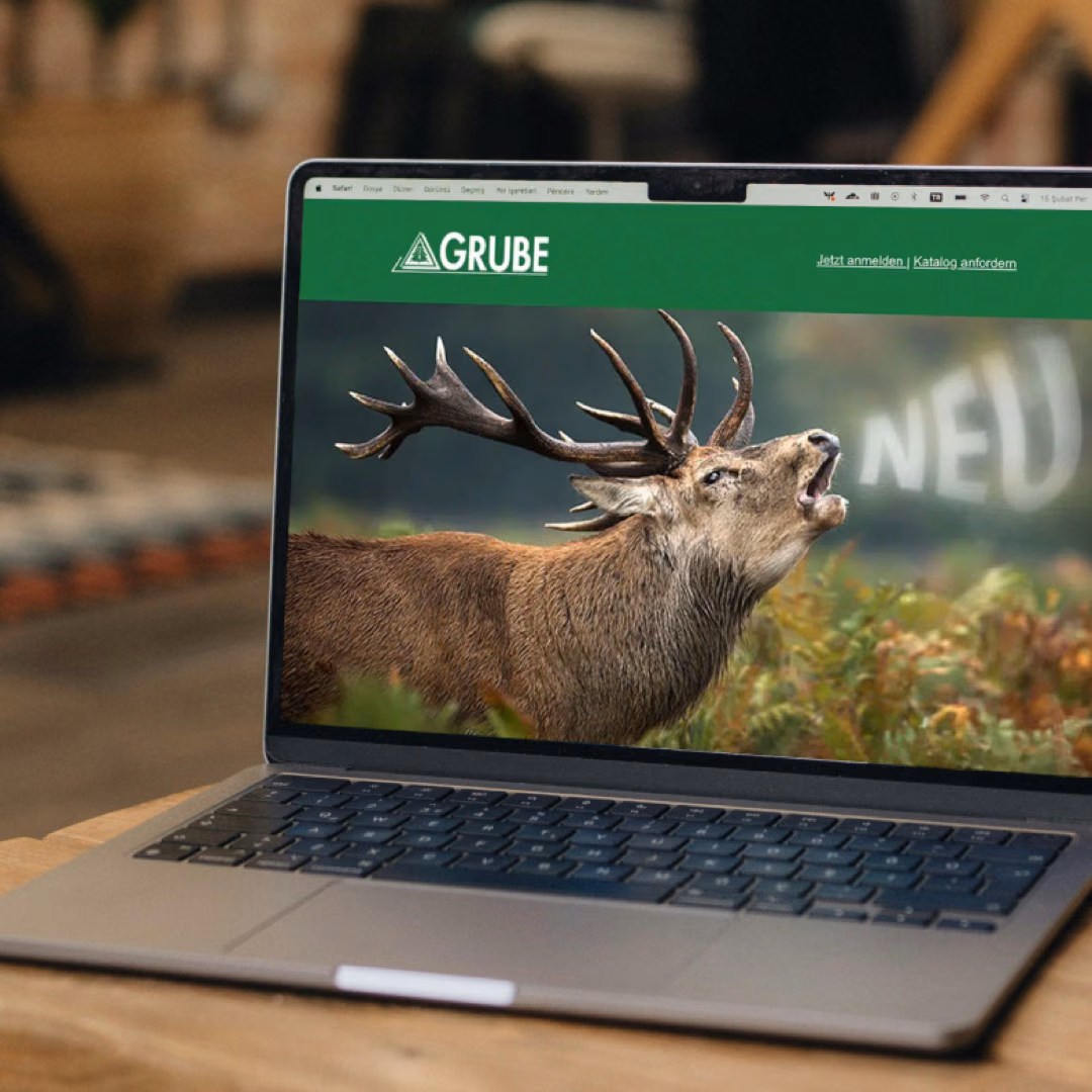 A laptop on a wooden table shows the Grube online shop, its homepage filled by a roaring red stag.