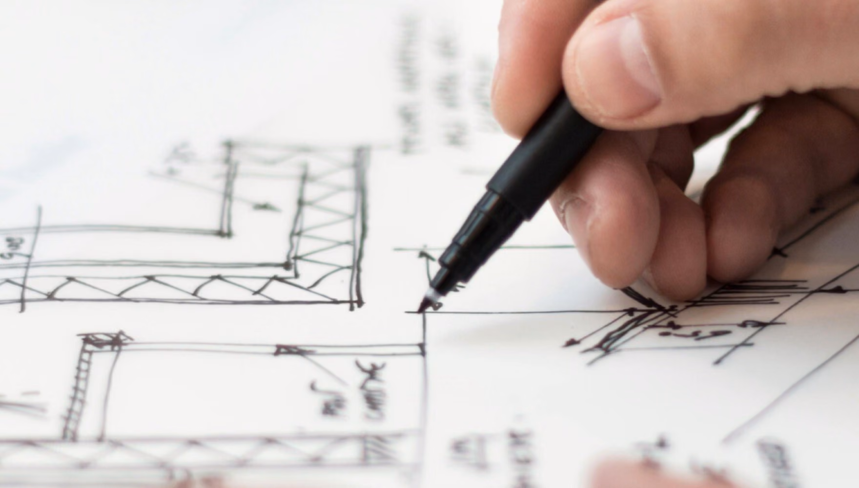 A hand redraws details on a sheet of hand-drawn plans with a black fineliner.