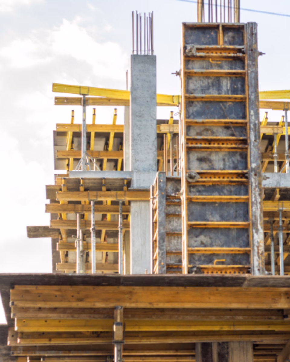 The top storey of a building under construction, timber and yellow beam formwork carrying the slab between bare concrete columns.