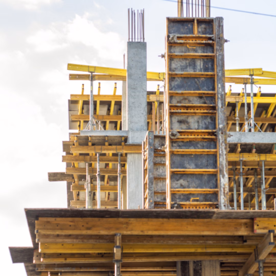 The top storey of a building under construction, timber and yellow beam formwork carrying the slab between bare concrete columns.
