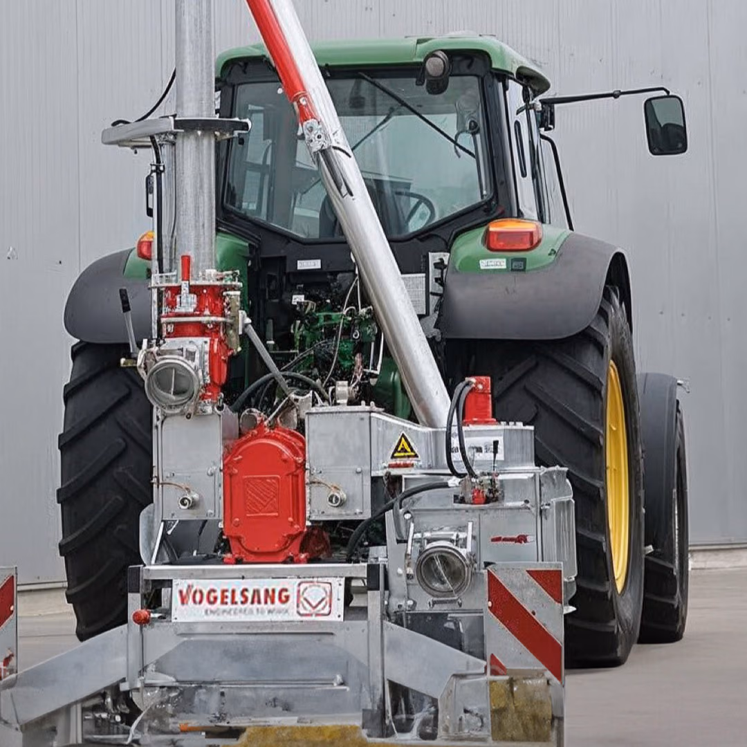 The rear of a green tractor carrying a mounted pump unit on a galvanised frame with the Vogelsang name across it, parked in front of a grey hall wall.