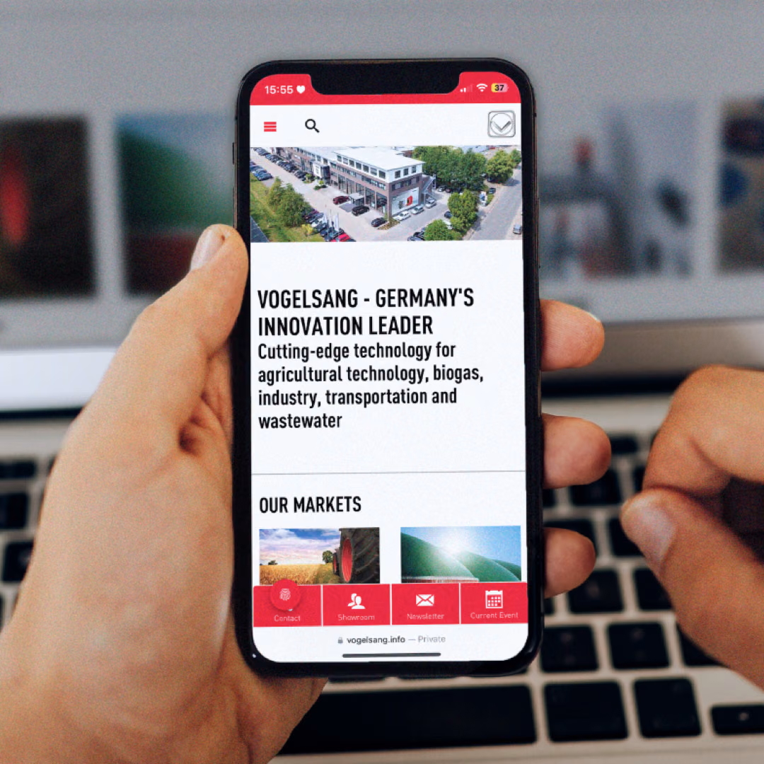 Two hands hold a phone showing Vogelsang's mobile site with an "our markets" list, in front of a laptop showing the same page in German.
