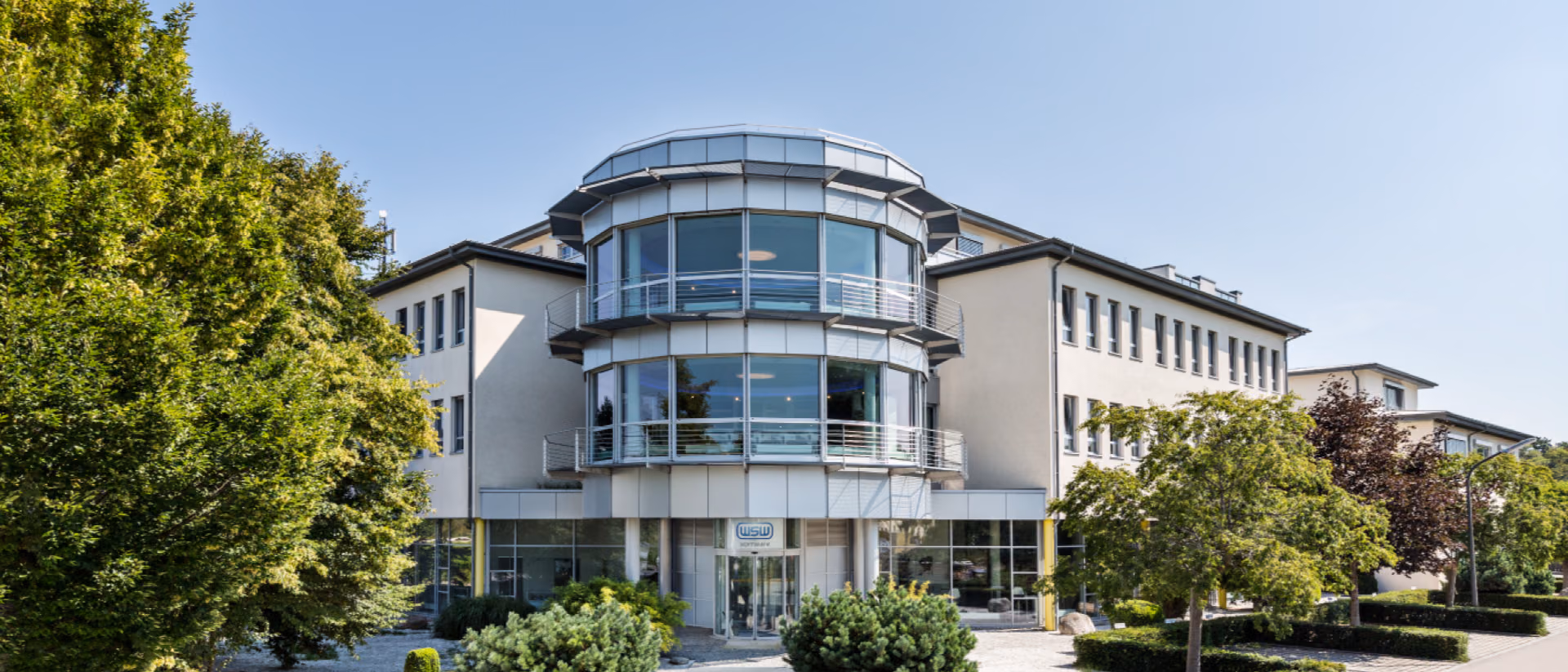 The WSW Software office building, three storeys with a rounded glass stair tower, behind clipped hedges and box balls.