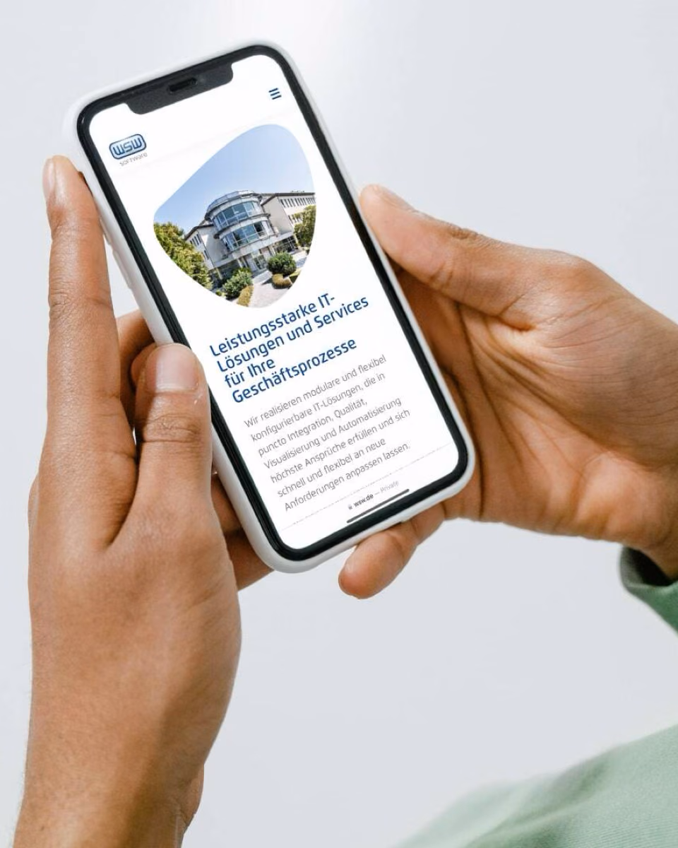 Hands hold a phone showing the WSW Software mobile site with a photograph of the company building.