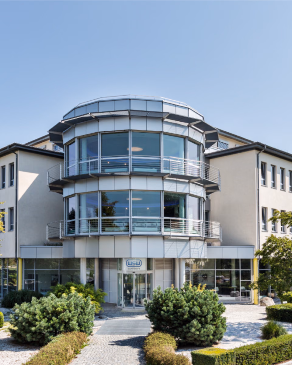 The WSW Software office building, three storeys with a rounded glass stair tower, behind clipped hedges and box balls.