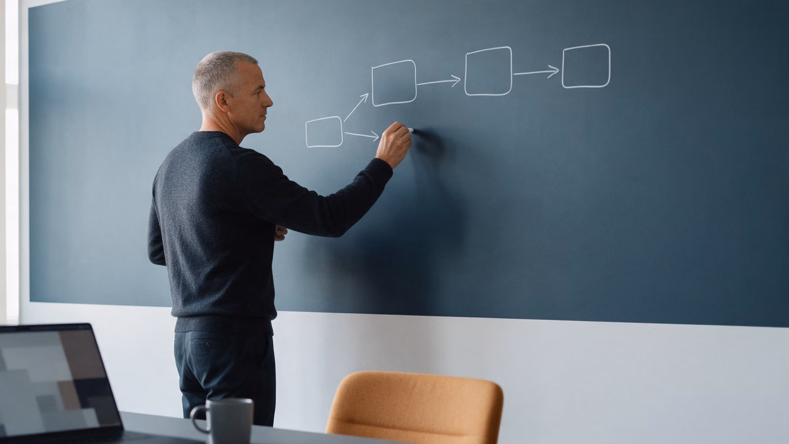Man drawing a flow of empty boxes and arrows on a dark writing wall.