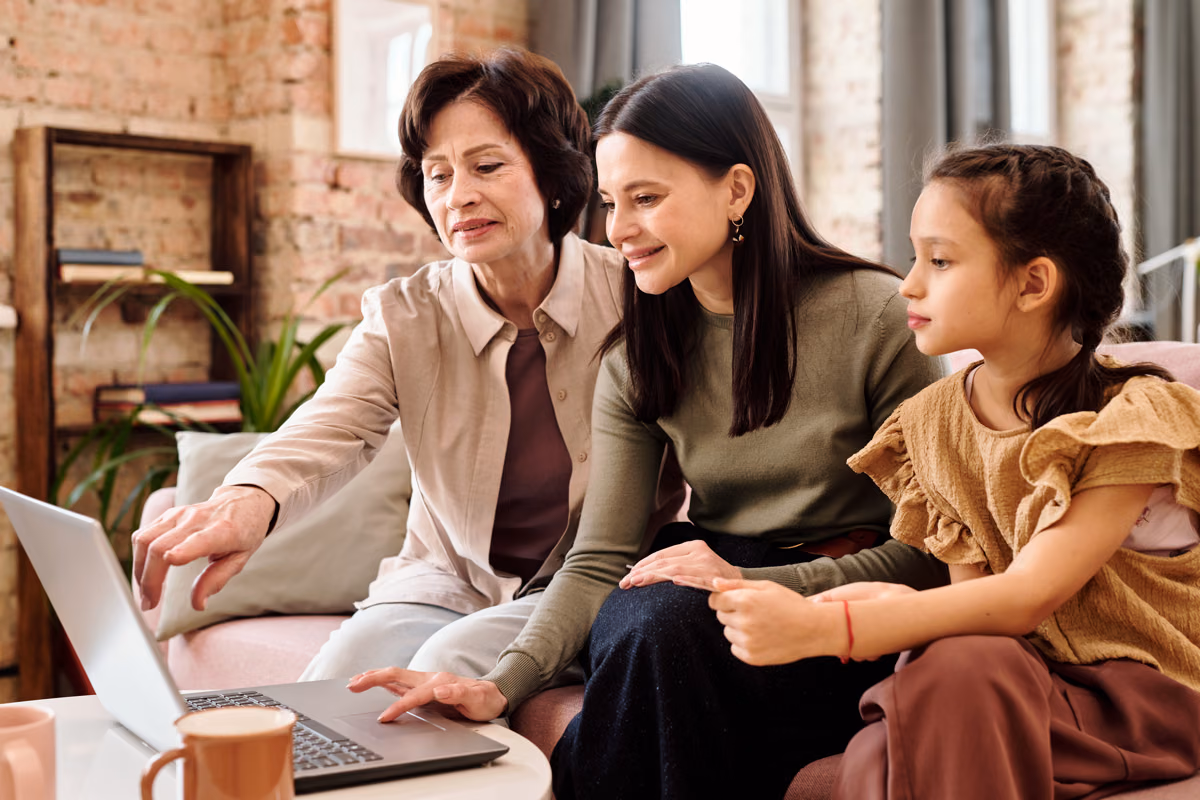 A young woman with a tablet in a meeting room, with older colleagues working at the table behind her.