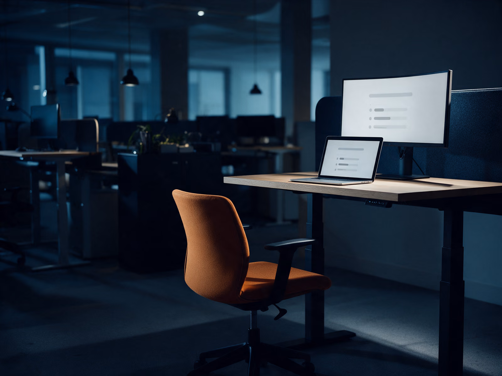 A tidy sit-stand desk at night, a curved monitor and a laptop showing several tasks progressing on their own.