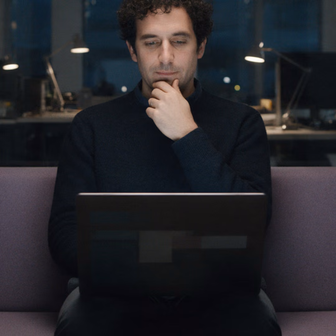 A man sitting in a focus booth after dark, working on a laptop with his hand at his chin.