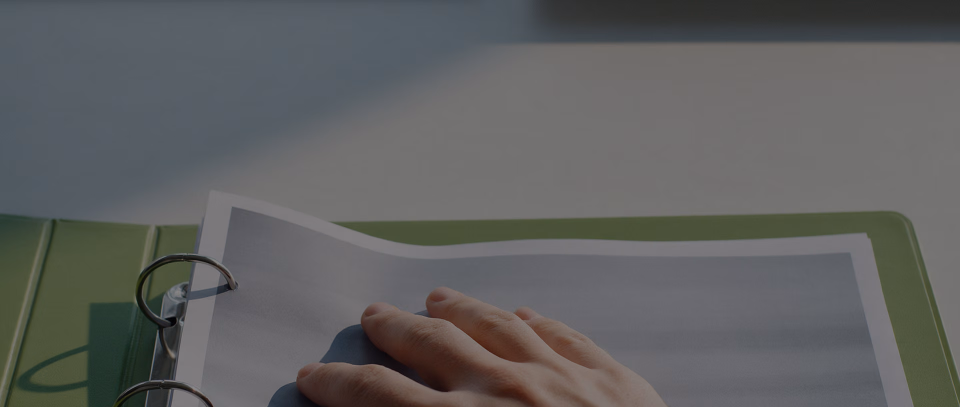 A close view of a hand pressing a printed sheet into an open green ring binder on a pale desk.